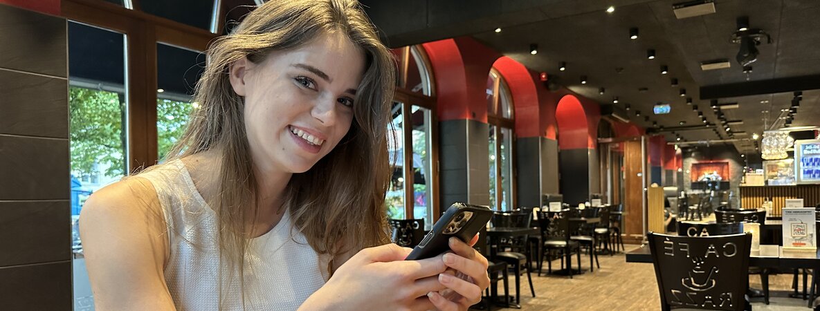 Alina Borgstrøm sitzt mit ihrem Smartphone in einem Café und lächelt.