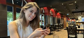 Alina Borgstrøm sitzt mit ihrem Smartphone in einem Café und lächelt.